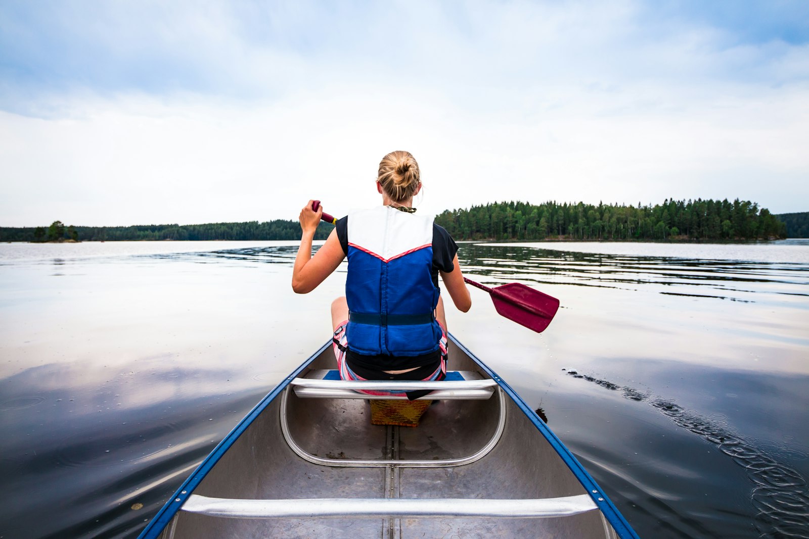 Padler i kano på et stille skogsvann med furukledde øyer (foto: Unsplash, fri kommersiell bruk)